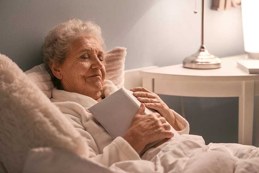 Senior woman with book sleeping in bed at night